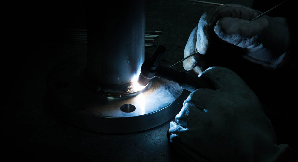 Welder carefully fillet welding a raised face flange to a stainless steel static mixer.